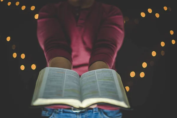Closeup shot of a person holding an open bible towards the camera with a blurred background — Stock Photo, Image