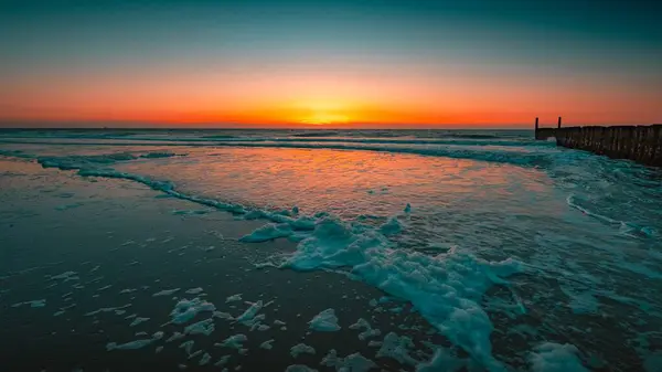 Magnifica vista dell'oceano schiumoso con tramonto sullo sfondo catturato a Domburg, Paesi Bassi — Foto Stock