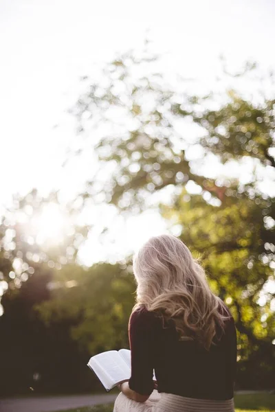 Vertikale Aufnahme einer Frau, die vor verschwommenem Hintergrund sitzt und die Bibel liest — Stockfoto