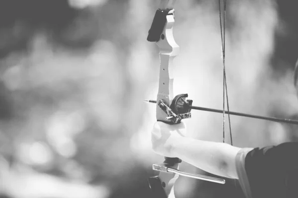 Close-up tiro de uma pessoa segurando um arco e flecha com um fundo borrado em preto e branco — Fotografia de Stock