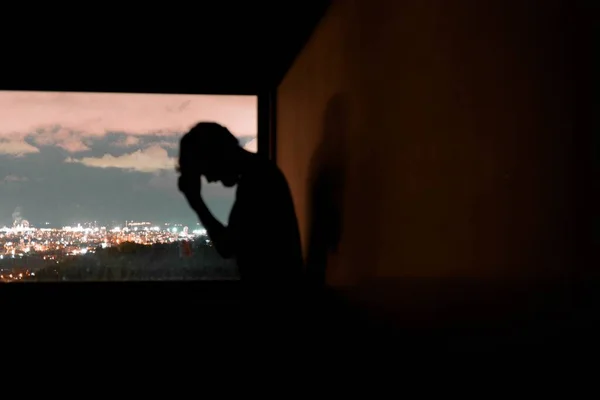 Silhouette einer depressiven Person, die nachts vor dem Hintergrund der Stadt denkt — Stockfoto