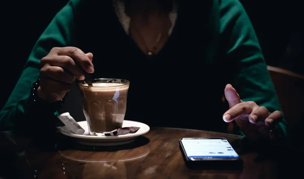 Крупним планом знімок жінки, що перемішує каву і використовує телефон — стокове фото