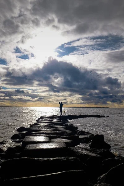 息をのむような曇り空の下で海の上に桟橋を形成岩の上に立っている男の美しいショット — ストック写真