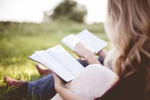 Photo de clôture de deux personnes assises dans un champ herbeux et remuant la bible sur un fond flou — Photo