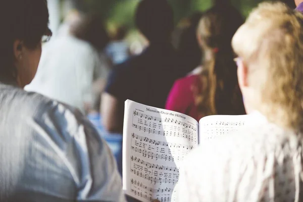 Selective focus shot from behind of people reading notes in the choir with a blurred background — Stock Photo, Image