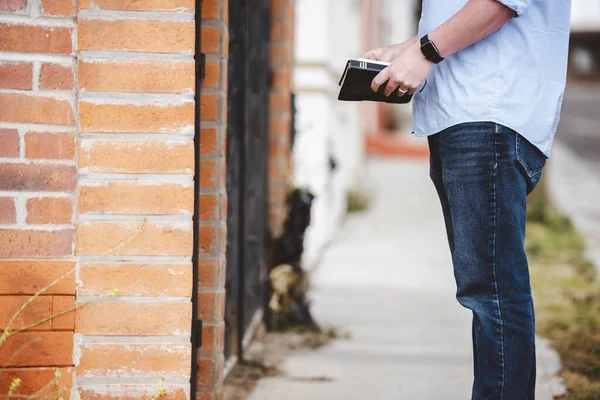 Primo piano di un maschio in piedi vicino a un edificio mentre tiene la Bibbia con uno sfondo sfocato — Foto Stock