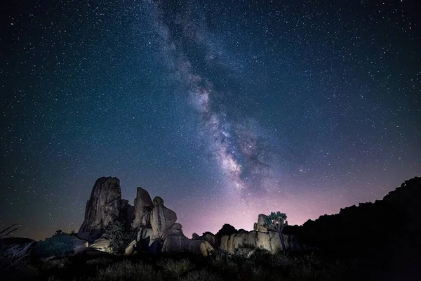 Belo tiro de silhuetas de rochas sob o céu roxo cheio de estrelas - papel de parede perfeito — Fotografia de Stock