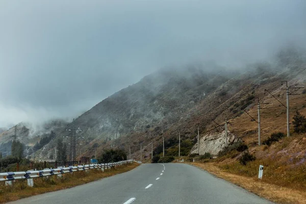 霧に包まれた高い山の近くの道路の美しいショット — ストック写真