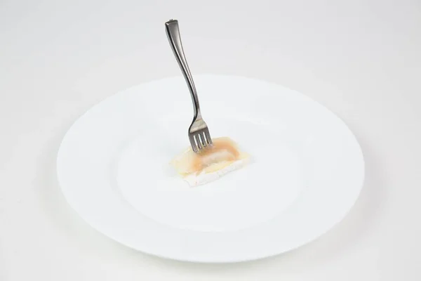 ภาพใกล้ชิดของส้อมติดอยู่ในชิ้นส่วนของปลาในจานสีขาวแยกกันบนพื้นหลังสีขาว — ภาพถ่ายสต็อก