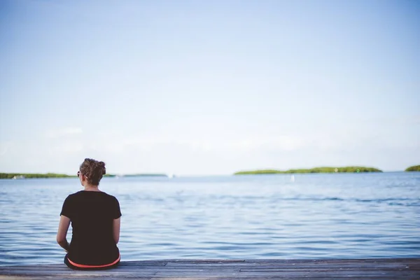 Vrouw zittend op een houten pad in de buurt van de zee met een wazig achtergrond schot van achteren — Stockfoto