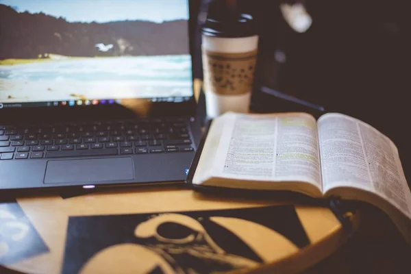 Selective focus shot of an open bible near laptop and coffee on the table with blurred background — Stock Photo, Image