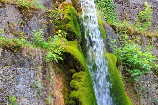 Gyönyörű lövés egy vízesésről, ami átjön a sziklákon, zöld mohával körülvéve. — Stock Fotó