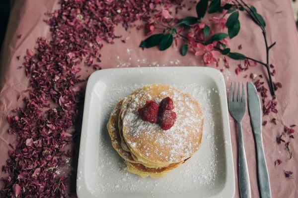 High angle shot of a delicious pancake with berries and pink flower petals on the ground