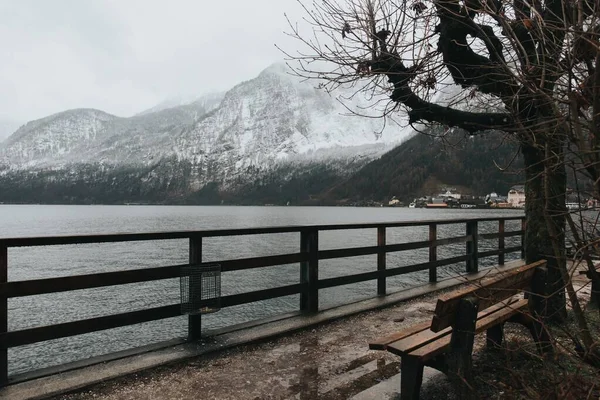 Piękne ujęcie ławki nad jeziorem w chłodny dzień i góry w tle — Zdjęcie stockowe