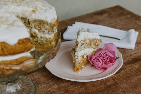 Closeup shot of a piece of a vanilla cake with a rose on the saucer and the shole cake next to it — Stock Photo, Image