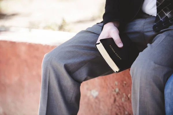 Close-up tiro de um macho sentado e segurando a bíblia com um fundo borrado — Fotografia de Stock