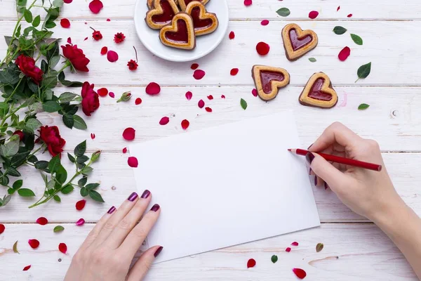 Person drawing on a white paper with a red pencil near heart-shaped cookies with rose petals — Stock Photo, Image