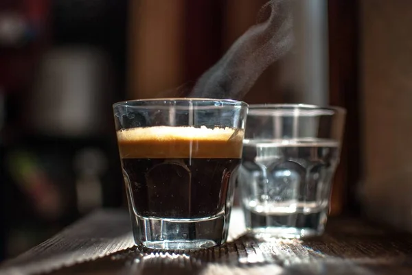 Primer plano de un vaso de café negro y un vaso de agua sobre una superficie de madera — Foto de Stock