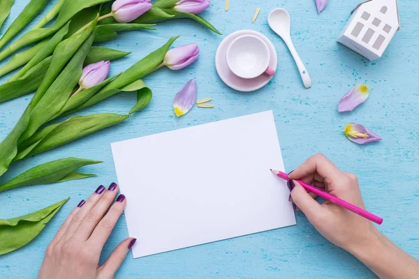 A person drawing on white paper with a pink pencil near purple tulips and a coffee cup — Stock Photo, Image