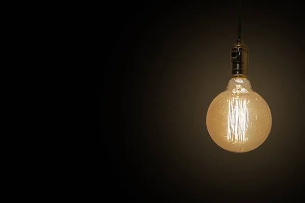 Tiro de close-up de uma lâmpada antiga iluminada isolada em um fundo preto - perfeito para um fundo — Fotografia de Stock