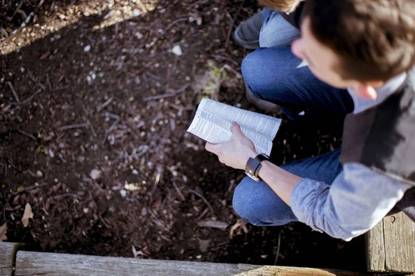 Overhead shot of a male sitting and holding the bible with a blurred background — Stock Photo, Image