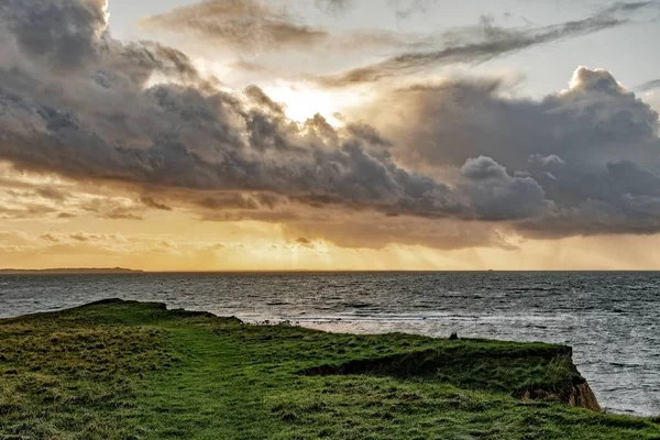 Vista deslumbrante de um penhasco coberto de grama sobre o oceano sob o belo céu nublado — Fotografia de Stock