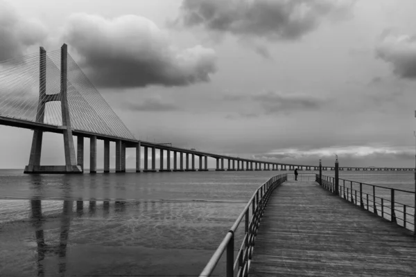 Человек, стоящий на пути через море с мостом Васко да Гама под облачным небом — стоковое фото