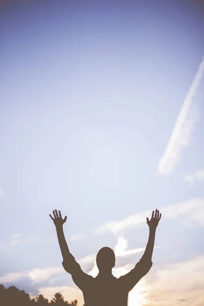 Silhouette of a person with its hands up towards the sky with blurred background in vertical shot — Stock Photo, Image