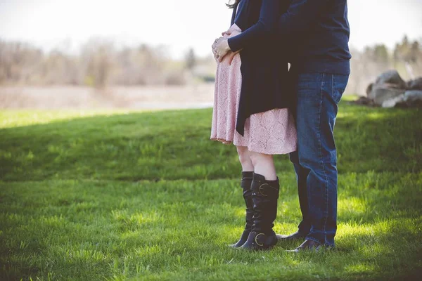 Closeup shot of a pregnant couple standing on a grassy field with a blurred background — Stock Photo, Image