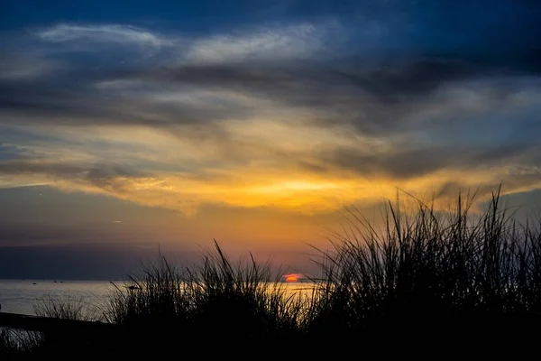Silhouette of a grassy field with the sea and a beautiful sky in the background at sunset