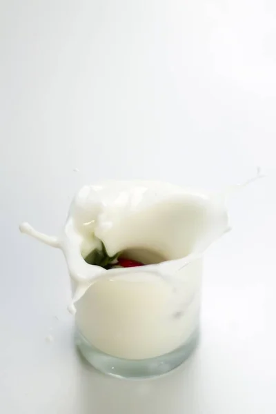 Вертикальний знімок полуниці, що бризкає у склянку молока на білому тлі — стокове фото