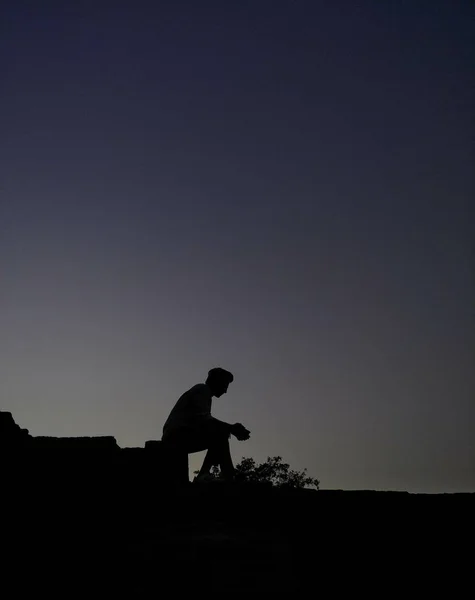 Vertical shot of a silhouette of a person sitting on a roof during evening time — Stock Photo, Image