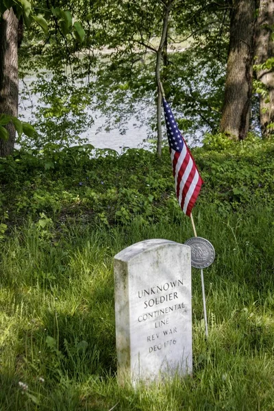 A vertical shot of a headstone dedicated to the unknown soldier with the American flag next to it