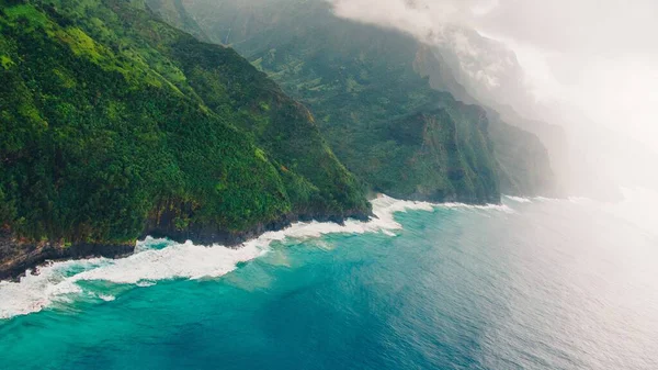 在夏威夷考艾岛捕捉到的平静的蓝色海洋上的美丽的雾状悬崖峭壁的高角镜头 — 图库照片