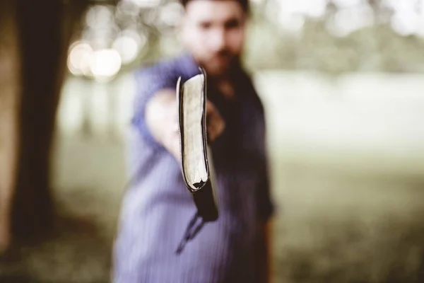 Zbliżenie Mężczyzny Trzymającego Biblię Stronę Kamery Zamazanym Tłem — Zdjęcie stockowe