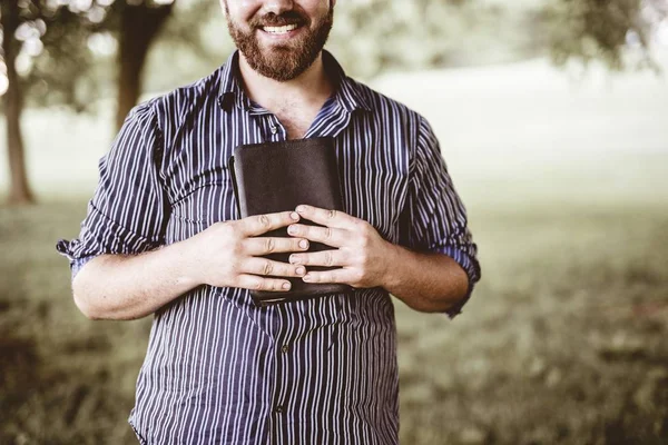 Close-up tiro de um macho sorrindo e segurando a bíblia com um fundo borrado — Fotografia de Stock