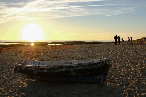 Beautiful shot of an old fishing boat and silhouettes of people on the beach during the sunset — Stock Photo, Image