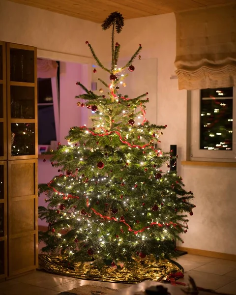 Árbol de Navidad bellamente decorado con adornos y luces de cuerda dentro de una habitación —  Fotos de Stock