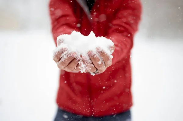 Close-up tiro de um macho segurando neve com suas duas mãos e um fundo borrado — Fotografia de Stock