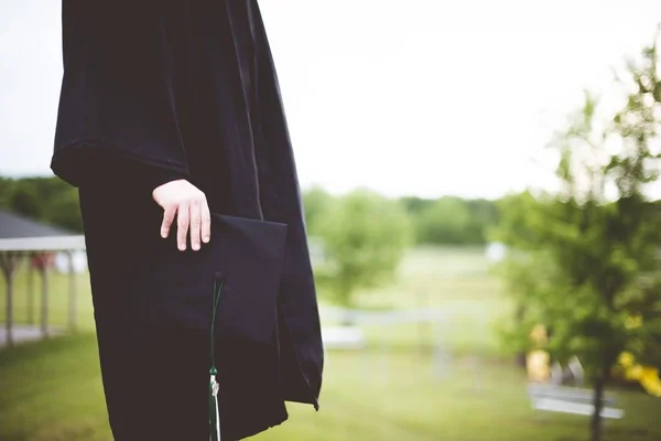 A shallow focus shot of a graduate holding its hat with a blurred background