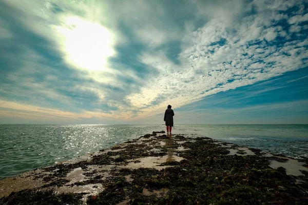 Schöne Aufnahme einer Person, die auf einem Land im Ozean unter dem wolkenverhangenen Himmel geht — Stockfoto