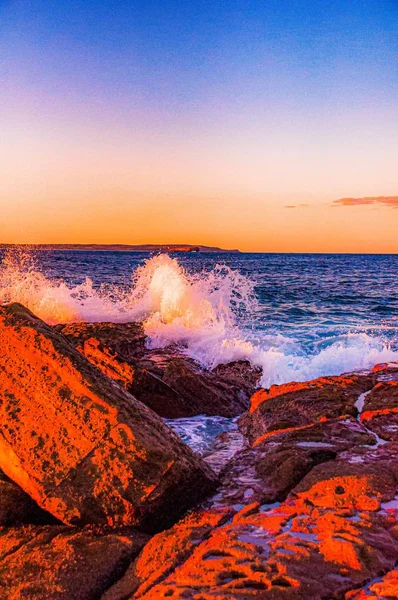 A vertical shot of waves splashing to the rock formations during a breathtaking sunset