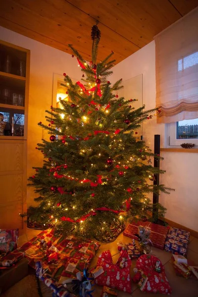 Massor av presenter under den dekorerade julgranen med prydnader och snörljus inne i ett rum — Stockfoto