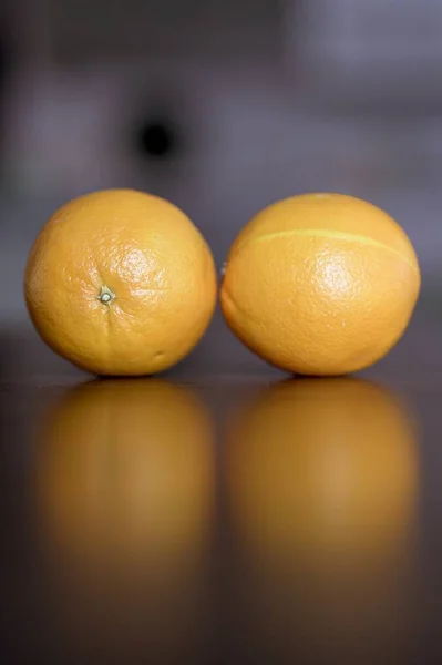 Vertikale Nahaufnahme von zwei Orangen auf einer Holzoberfläche mit unscharfem Hintergrund — Stockfoto