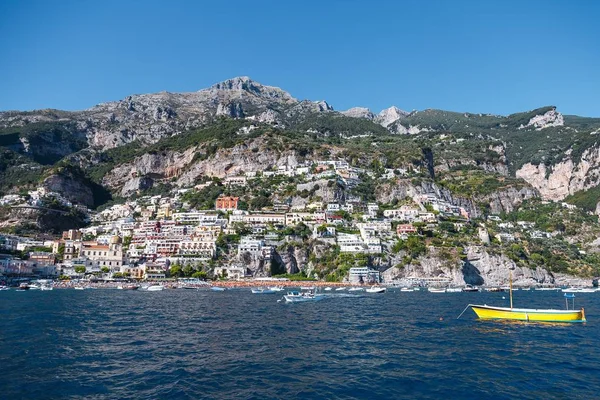 A yellow boat on the sea near a lot of buildings on the hill in Sorrento, Italy