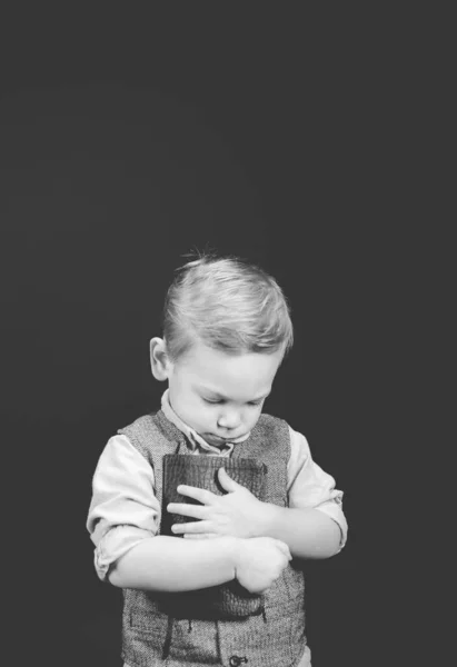 Vertical grayscale shot of a child holding the bible with his eyes closed — Stok Foto