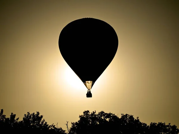 Silhueta de um balão no céu acima das árvores com o sol no fundo — Fotografia de Stock