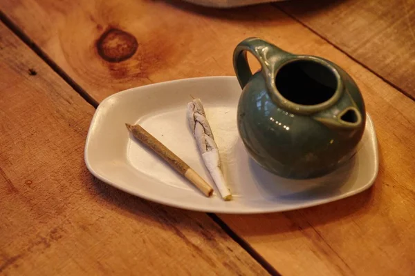 Alto ángulo de primer plano de una tetera y cigarrillos en un plato blanco sobre una superficie de madera —  Fotos de Stock