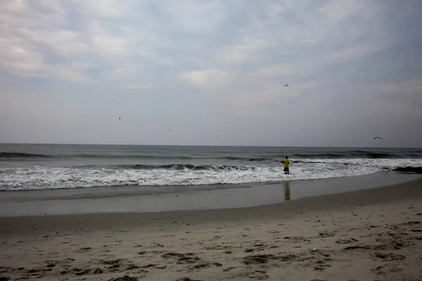 一个身穿黄色T恤衫的人站在海滨享受这美妙的一天 — 图库照片