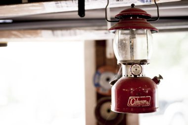 JACKSON, UNITED STATES - Jan 01, 2019: Old Colman lamp hanging in a garage. The window is seen behind a little blurred out. clipart